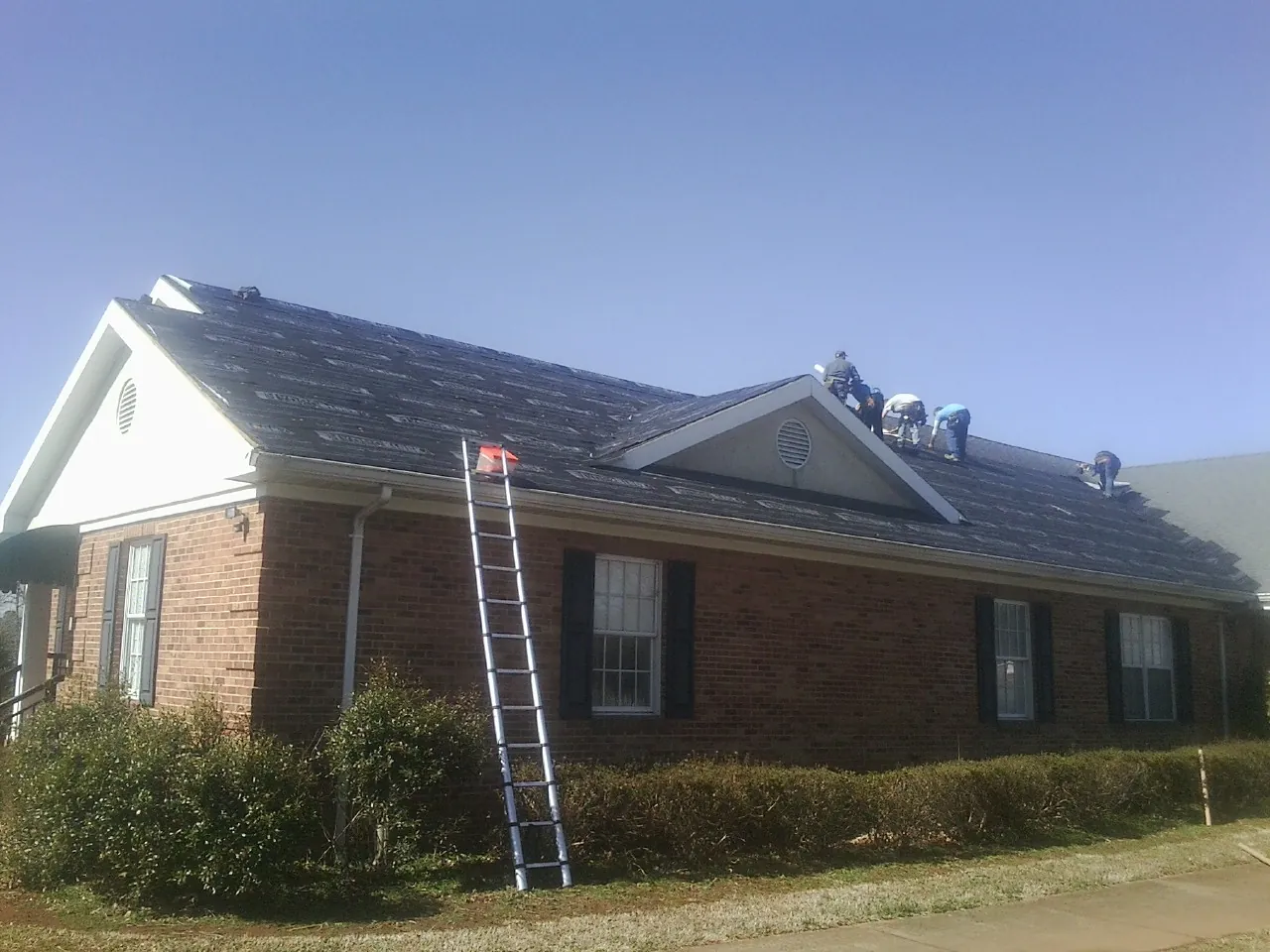 Crew tearing shingles off a brick ranch roof with a ladder set — Emergency Roof Repair work by our crew in Ulm