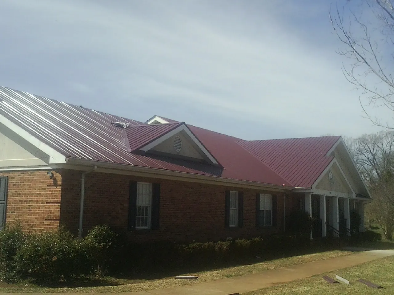 Red metal roof with gabled entries on a long brick building, from a Hail Damage Roof Repair job in Ulm