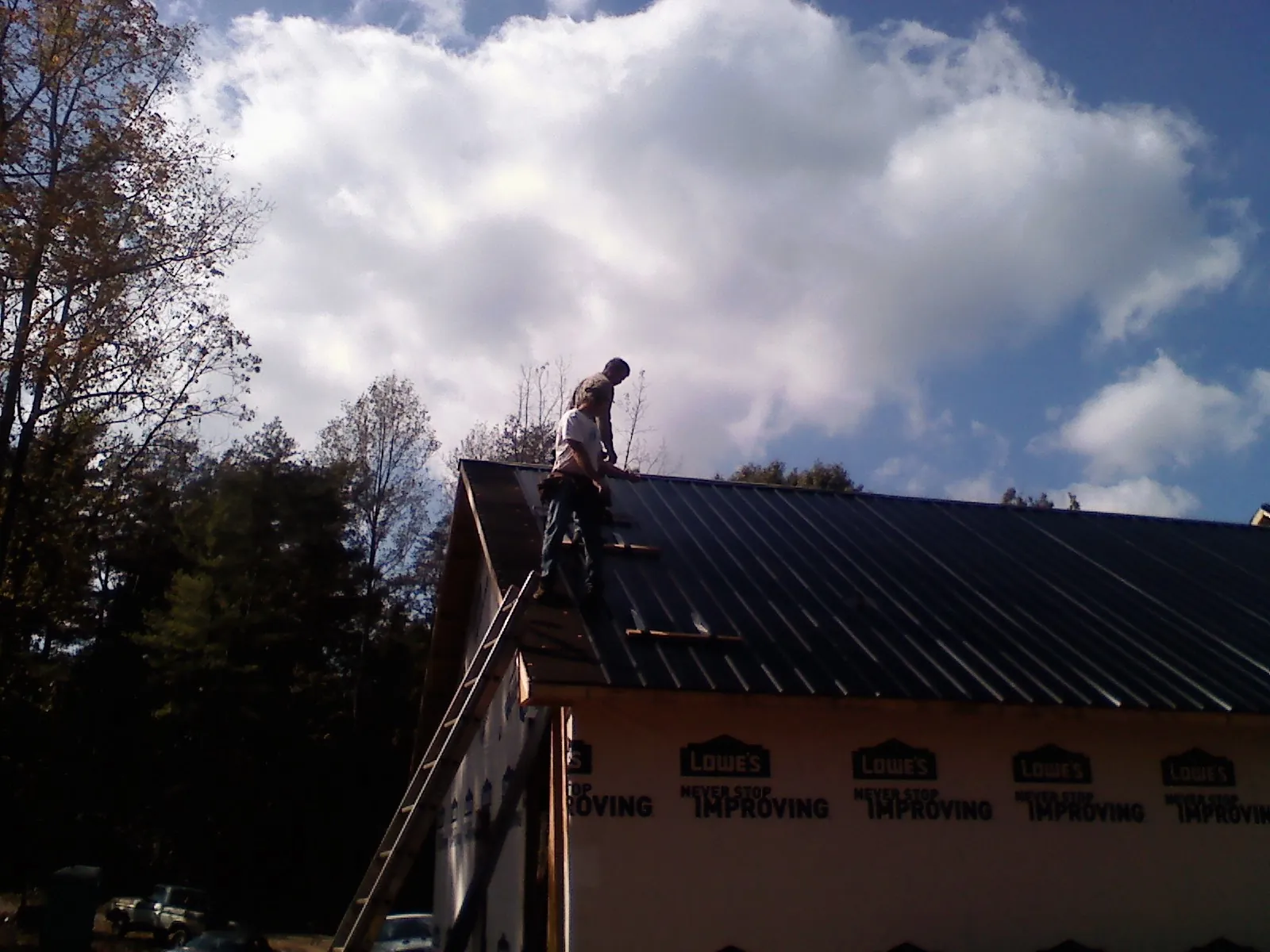 Roofer fastening dark metal panels high against a cloudy sky, from a Roof Inspection job in Ulm