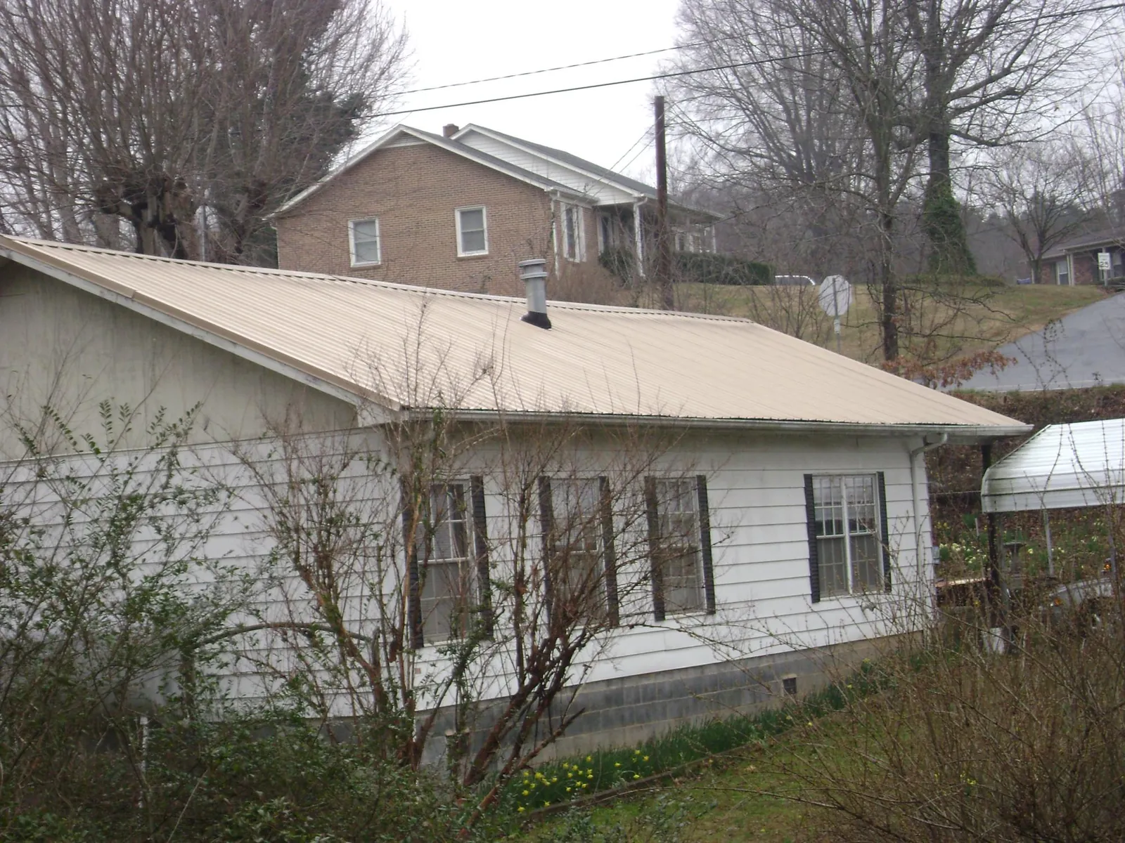 Tan metal roof on a white sided house set into a hillside — Commercial Roofing by Roofing Brothers in Ulm